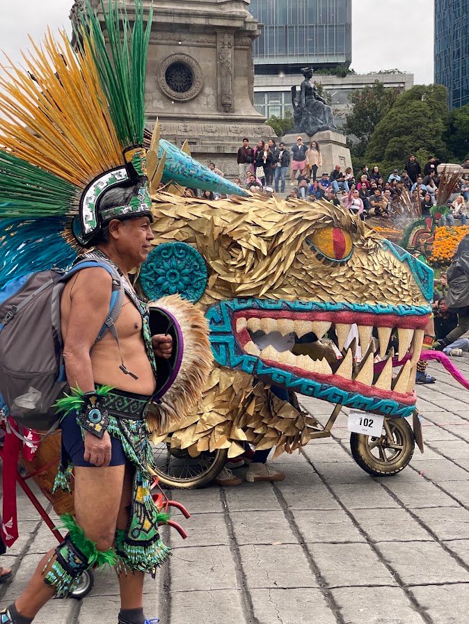 Danseur en coiffe de plumes à côté d'un alebrije jaguar doré devant l'Ange de l'Indépendance